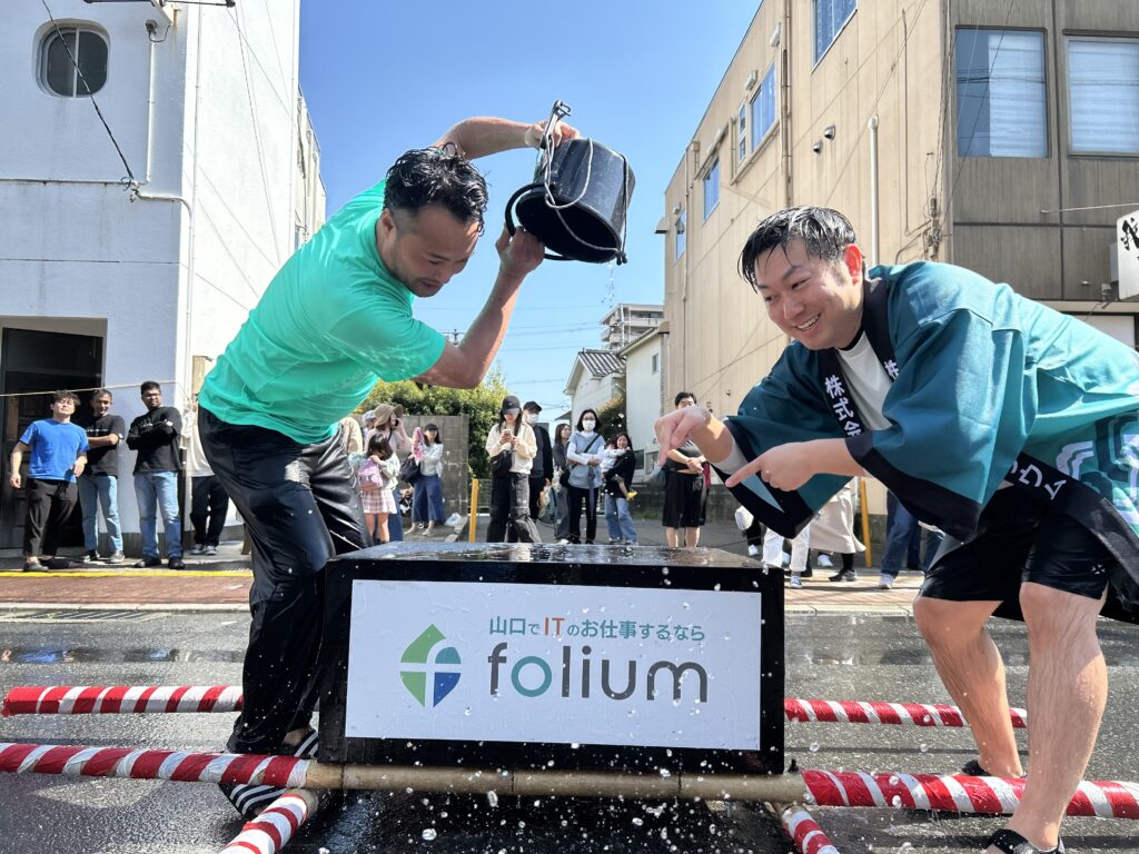 フォリウムのロゴ神輿に温泉をぶっかける取締役石井（左）とマネージャー（右）