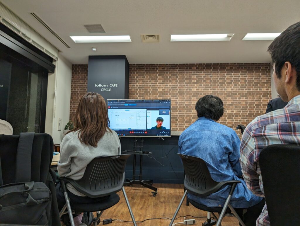 八戸のオフィスからリモートでプレゼンを行う横山（中央モニター内）