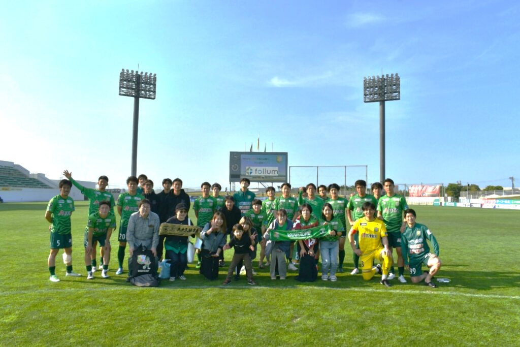 ピッチ内でヴァンラーレ八戸FCの選手と記念撮影するフォリウム社員とその家族